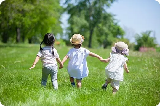 草原で手をつないで走る3人の子どもたち