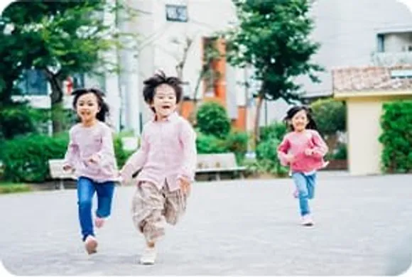 広場を笑顔で走る3人の子どもたち