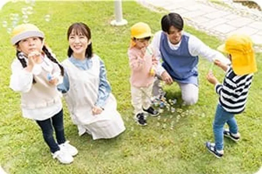 芝生でシャボン玉遊びをする先生と園児たち