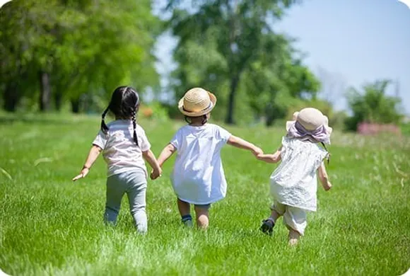 草原で手をつないで走る3人の子どもたち