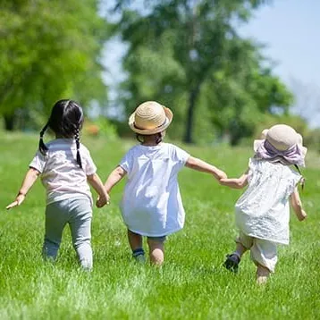 草原で手をつないで走る3人の子どもたち