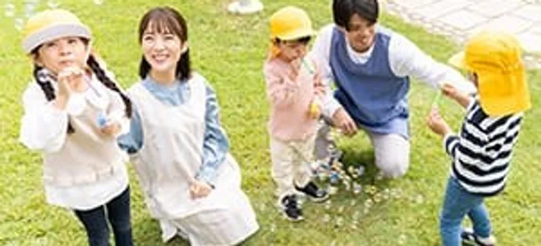 芝生でシャボン玉遊びをする先生と園児たち