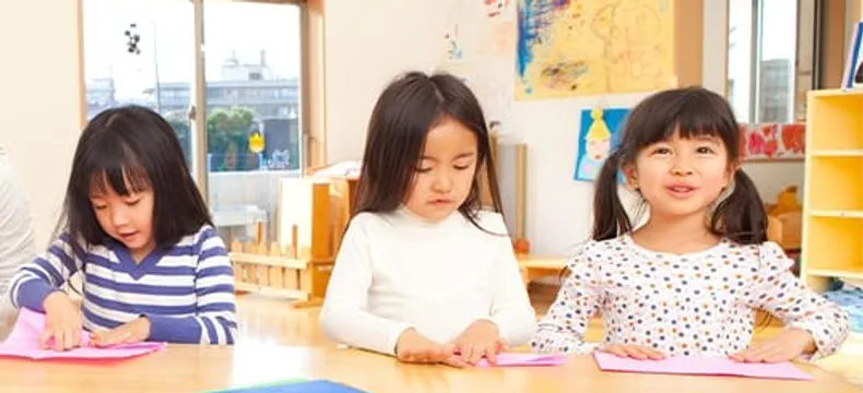 教室で折り紙をする3人の園児